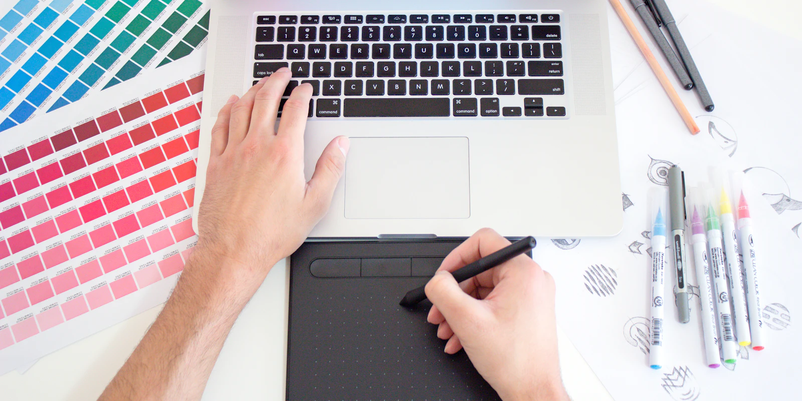 A designer working with a drawing tablet, a laptop, and color swatches