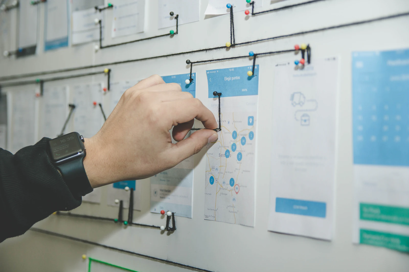 A hand pinning printed app screens into a flow map on a wall