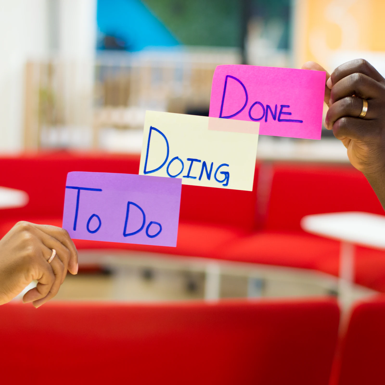 Hands holding three sticky notes labeled To Do, Doing, and Done