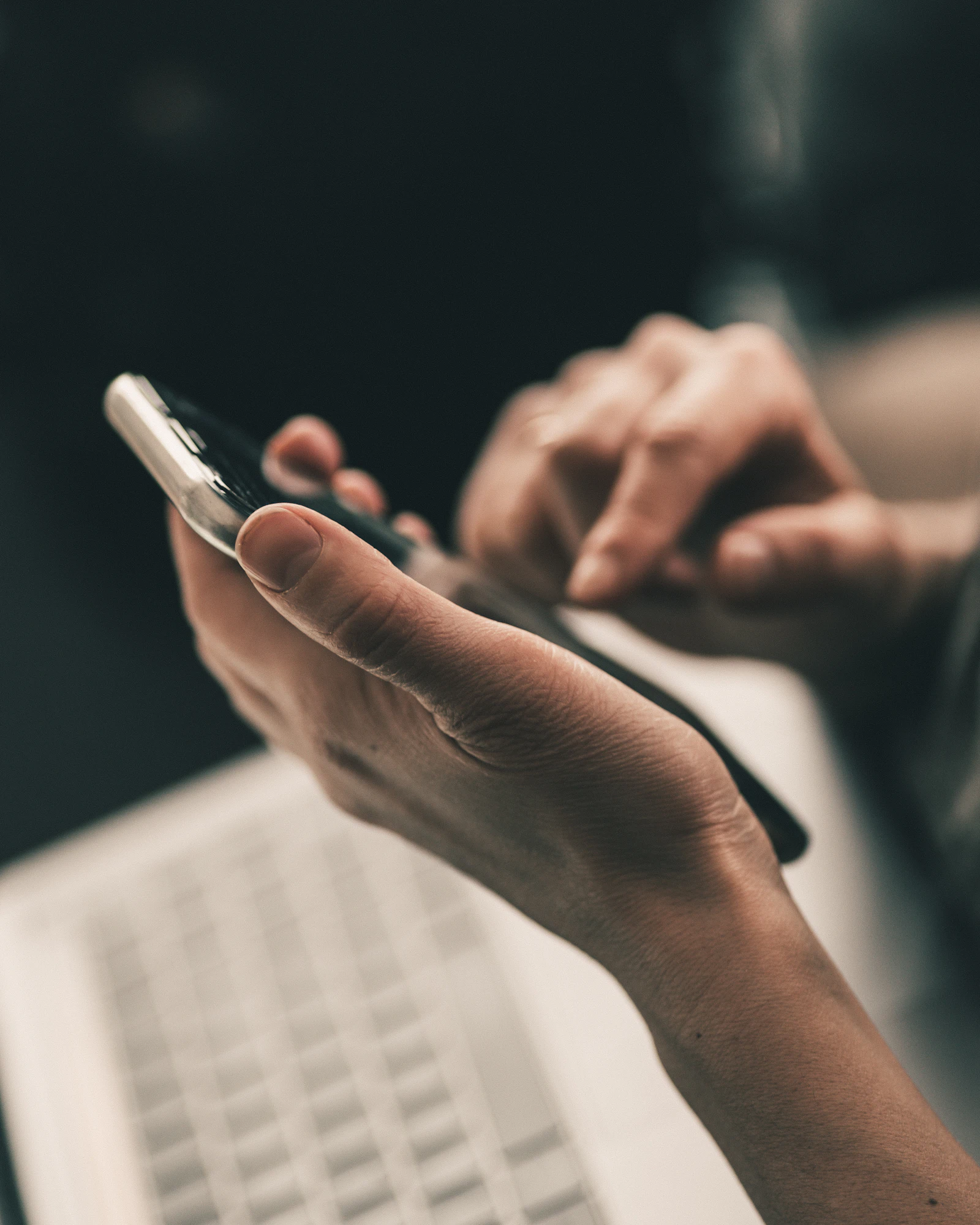 A hand holding a phone above a laptop keyboard