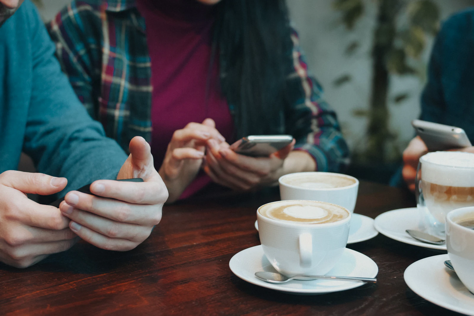 Three people using their phones at a table with cups of coffee