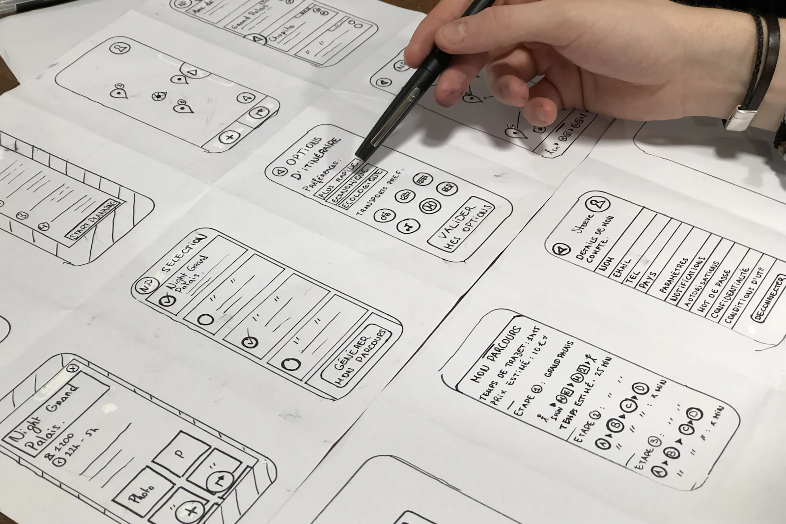 A hand sketching mobile app screens on sheets of paper