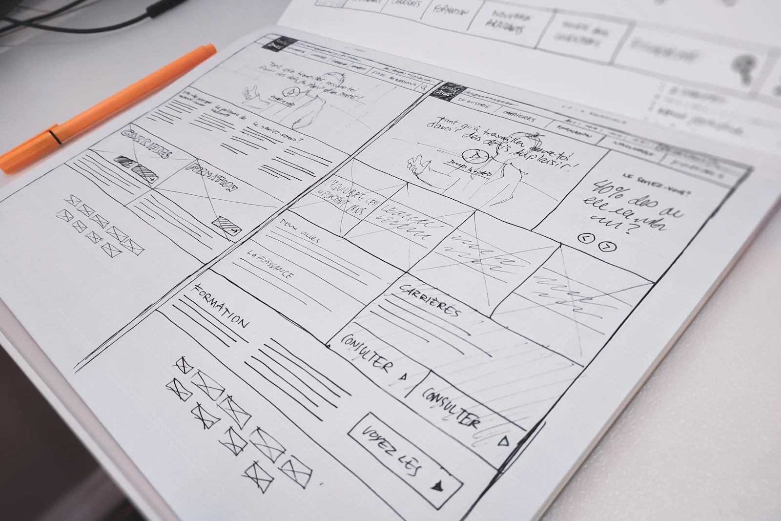 A hand-drawn website wireframe on paper next to an orange pen